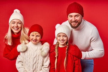 Fototapeta premium young family in sweaters, isolated on red wall background. beautiful happy parents with daughter and son smile, portrait