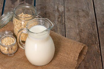 Glass pitcher of milk and oat flakes on wooden table