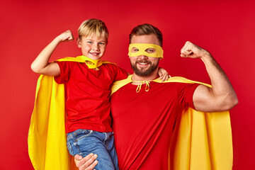brave and strong father with son in superhero costume, they show arm muscles at camera, wearing...