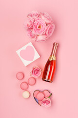 Flowers, bottle of wine, sweets and gift on pink background. Valentines day concept. Flat lay, top view, copy space.