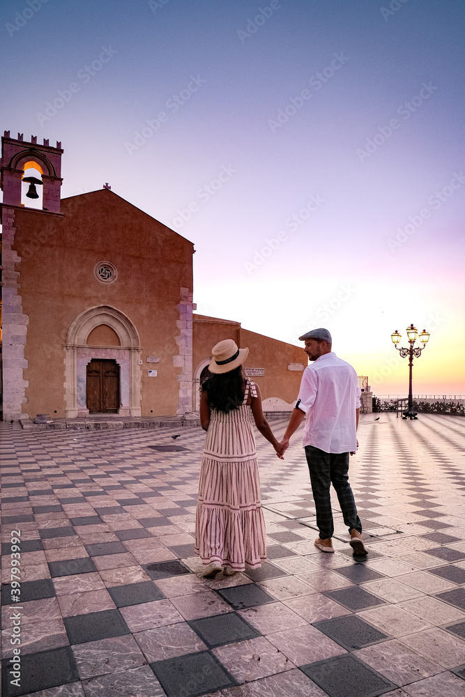 Wall mural taormina sicily, couple men and woman mid-age watching the sunrise at the old town of taormina sicil