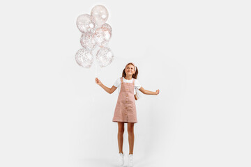 Full length photo of beautiful happy little girl holding balloons celebrating a festive event over isolated white background