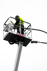 a repairman in overalls on a tower repairing a road lamp. Electrical repair man at work fixing a street light.