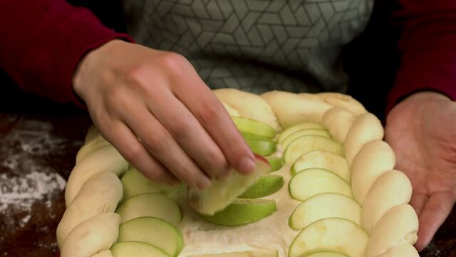 Process of making an apple pie. Stock footage. Close up of cooking tasty dessert, raw pastry with apple slices before baking , female hand taking one apple slice.