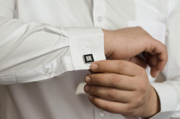 Groom's hands fasten the black cufflinks on his shirt, close-up. The preparations of the groom