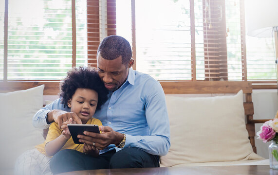 Portrait Of American African Father And Son Using Gadget Learning At Home. Daddy And His Little Boy Spending Leisure Time At Home. Single Dad, Family Lifestyle Father's Day Concept