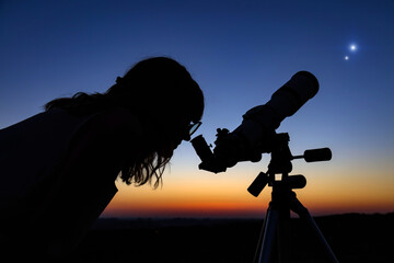 Woman looking at night sky with amateur astronomical telescope.