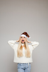 scared caucasian girl with long fair hair in white sweater, blue jeans and red christmas hat