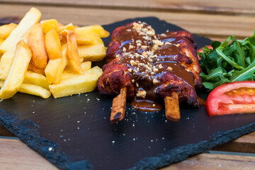 American fast food. A couple of beef and chicken skewers with a delicious peanuts sauce with some fresh salad with tomatoes and crunchy french fries. Delicious meat steaks on a wooden background