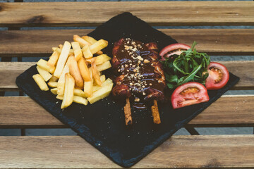 American fast food. A couple of beef and chicken skewers with a delicious peanuts sauce with some fresh salad with tomatoes and crunchy french fries. Delicious meat steaks on a wooden background