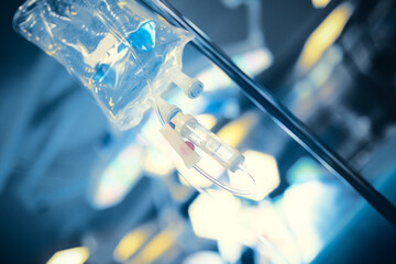 Intravenous drip on the steel medical pole against the blurred surgical light