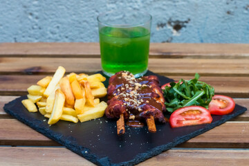 American fast food. A couple of beef and chicken skewers with a delicious peanuts sauce with some fresh salad with tomatoes and crunchy french fries. Delicious meat steaks on a wooden background