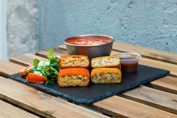Classic, Italian arancini. deep fried Rice balls with minced meat and some vegetables inside. Tasty crunchy food with peanuts sauce and tomatoes soup with mozzarella cheese on the top. Close up view