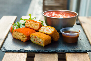 Classic, Italian arancini. deep fried Rice balls with minced meat and some vegetables inside. Tasty crunchy food with peanuts sauce and tomatoes soup with mozzarella cheese on the top. Close up view
