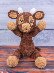 Plush bull toy on a wooden background. Soft toy with raised legs. Symbol of 2021 New Year.