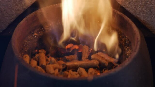 Round pellets of biofuel for burning in a home wood stove. made from sawdust and shredded paper. in closeup. Heated pellet stove cylinder filled with alternative biofuel throwing out fire sparkles
