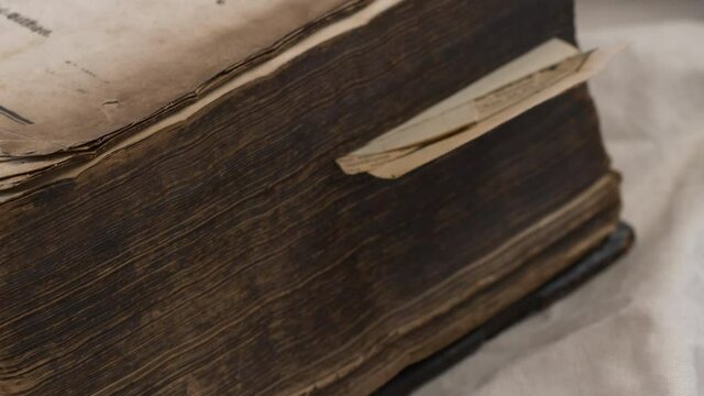 Close pan along ancient heavy worn bible in Swedish on white sheet