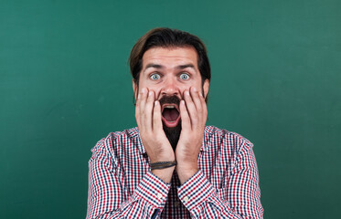 surprised mature bearded man teacher in school classroom with blackboard, back to school