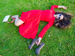 Relaxed young person teenage girl lying in grass. Teen girl brunette in red dress with a drink...