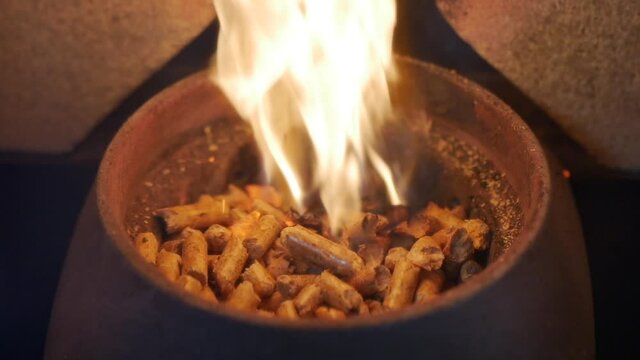 Slow motion burning wooden pellets in pellet stove. Alternative biofuel heating houses, renewable biomass. Ecological bio granules used for warming buildings in cold weather. Heated pellet stove