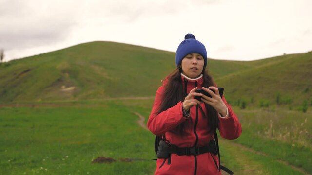 Free Young woman tourist blogger records selfie video at foot of mountains using smartphone against backdrop of beautiful landscape. Healthy cheerful girl travels and takes pictures of nature by phone