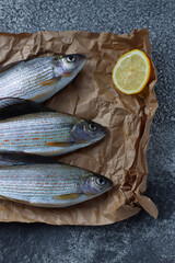 Freshly caught grayling with lemon slices is on parchment paper on the table. Freshwater fish. Preparation for cooking. Top view