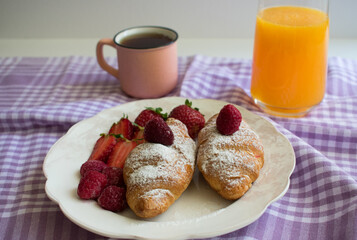 Fresh croissant and strawberries on a white plate.