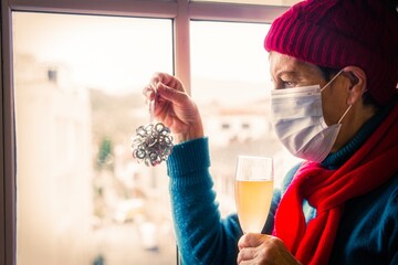 senior woman with disposable surgical mask placing christmas decorations and toasting with champagne at christmas and new year