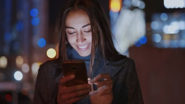 Closeup of prety smiling woman using smartphone walking at night city, slowmotion fullHD stock footage, handheld camera shot, clip has noise