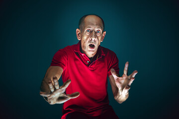 Fototapeta premium Ready to defend. Portrait of crazy scared and shocked caucasian man isolated on dark background. Copyspace for ad. Bright facial expression, human emotions concept. Watching horror on TV, cinema.