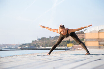 middle-aged female doing yoga asana on one leg on the sunny beach at plank f