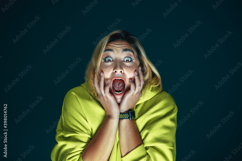 Wall mural screaming. portrait of young crazy scared and shocked caucasian woman isolated on dark background. c