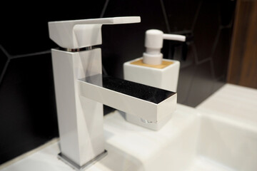 white square faucet with a white container for liquid soap in the bathroom side view