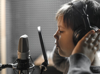 Boy in check shirt and headphone is singing or talking into microphone with pop filter in voice...