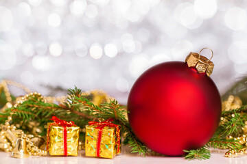 Red Christmas ball. Nearby is a tree branch and New Year's decorations. Blurred background of silver color