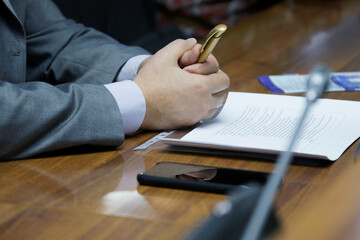 A man in a business suit sits at a table in front of a speakerphone. Meeting, seminar, or...