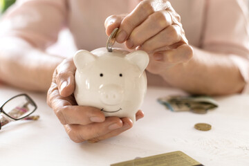 Hands of old women's put money coins in a piggy Bank, the concept of retirement.