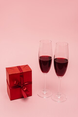 red wine in glasses near gift isolated on pink
