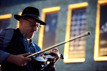 Portrait of a street musician man in a hat with a violin in the city.