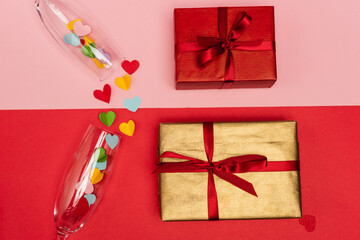 top view of champagne glass with hearts near gifts on pink and red background