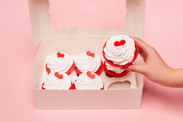 cropped view of woman holding valentines cupcake near box on pink background