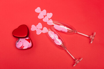 top view of pink hearts in champagne glasses near box on red background