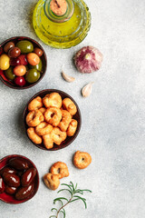 Tarallini-traditional Italian small bagels. Taralli. Tasty snack. Black and green olives, Kalamata, olive oil, garlic and rosemary on a grey concrete background. Selective focus, copy space