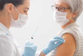 Doctor giving a senior woman a vaccination - obrazy, fototapety, plakaty