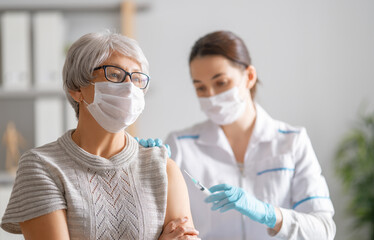 Doctor giving a senior woman a vaccination - obrazy, fototapety, plakaty