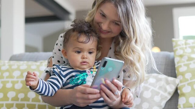 Young mom with baby girl playing with smartphone