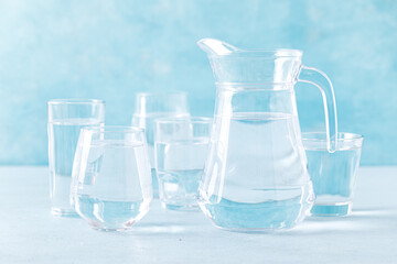 Water in glasses and a glass pitcher on a table on blue background