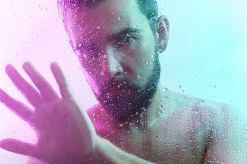 Portrait of handsome man through wet glass in neon light