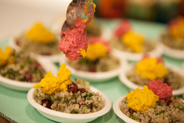Someone decorating Finger food Quinoa Bowl with pink and yellow humus with two spoons on a plate