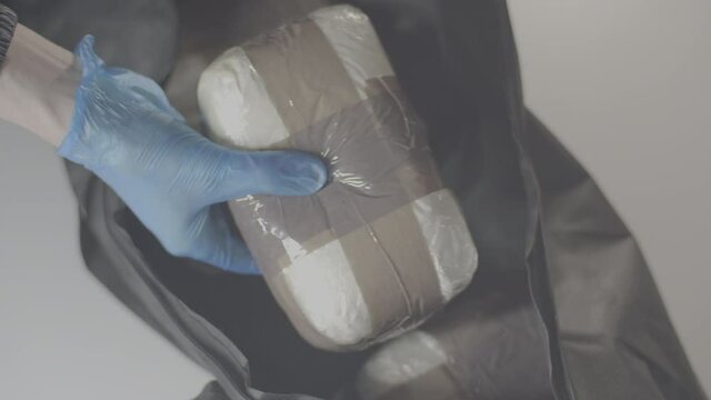 Police Officer picking up cocaine parcels from black bag 